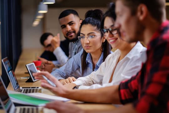 Professional training program featuring a group of individuals collaborating on laptops in a classroom and professionals working outdoors, with text highlighting 'Complete Practical Training' and '100% Job Assistance' for career support.